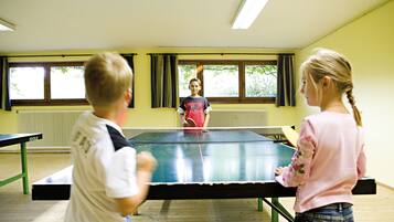 Una habitación con mesa de ping pong, una ventana con cortinas y un radiador.