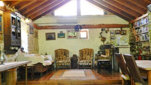 A cozy attic room with wooden beams, a large window, and a bookshelf filled with books. - Daphne House (Kumluca)