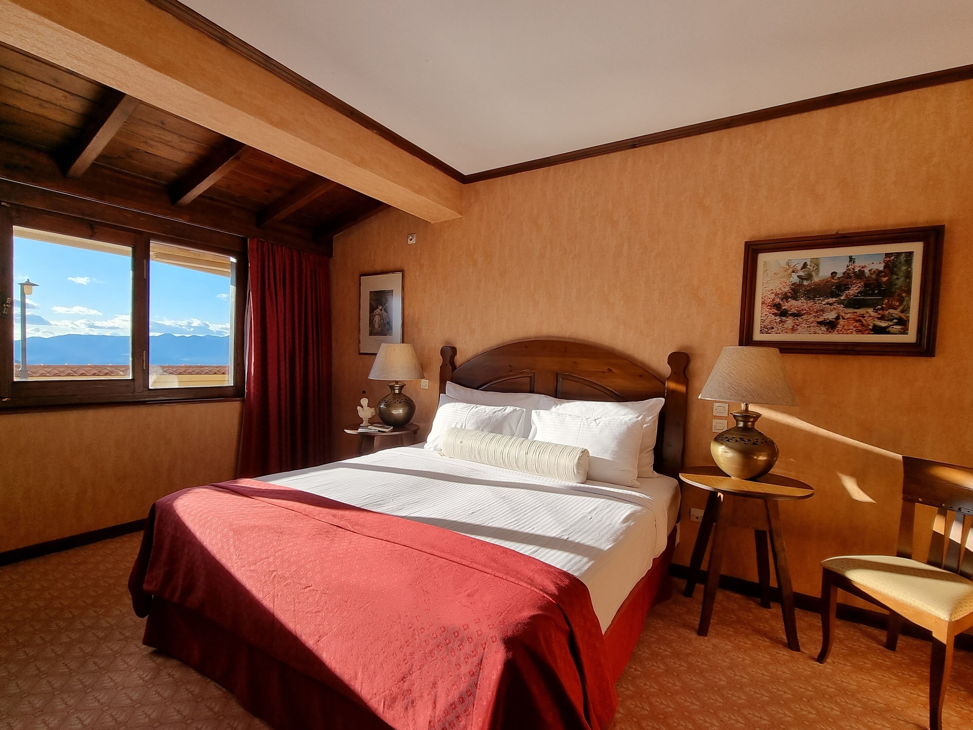 Ein Hotelzimmer mit einem großen Bett, einem Sessel, einem Tisch, einem Fenster mit Vorhängen und einem Bild an der Wand.