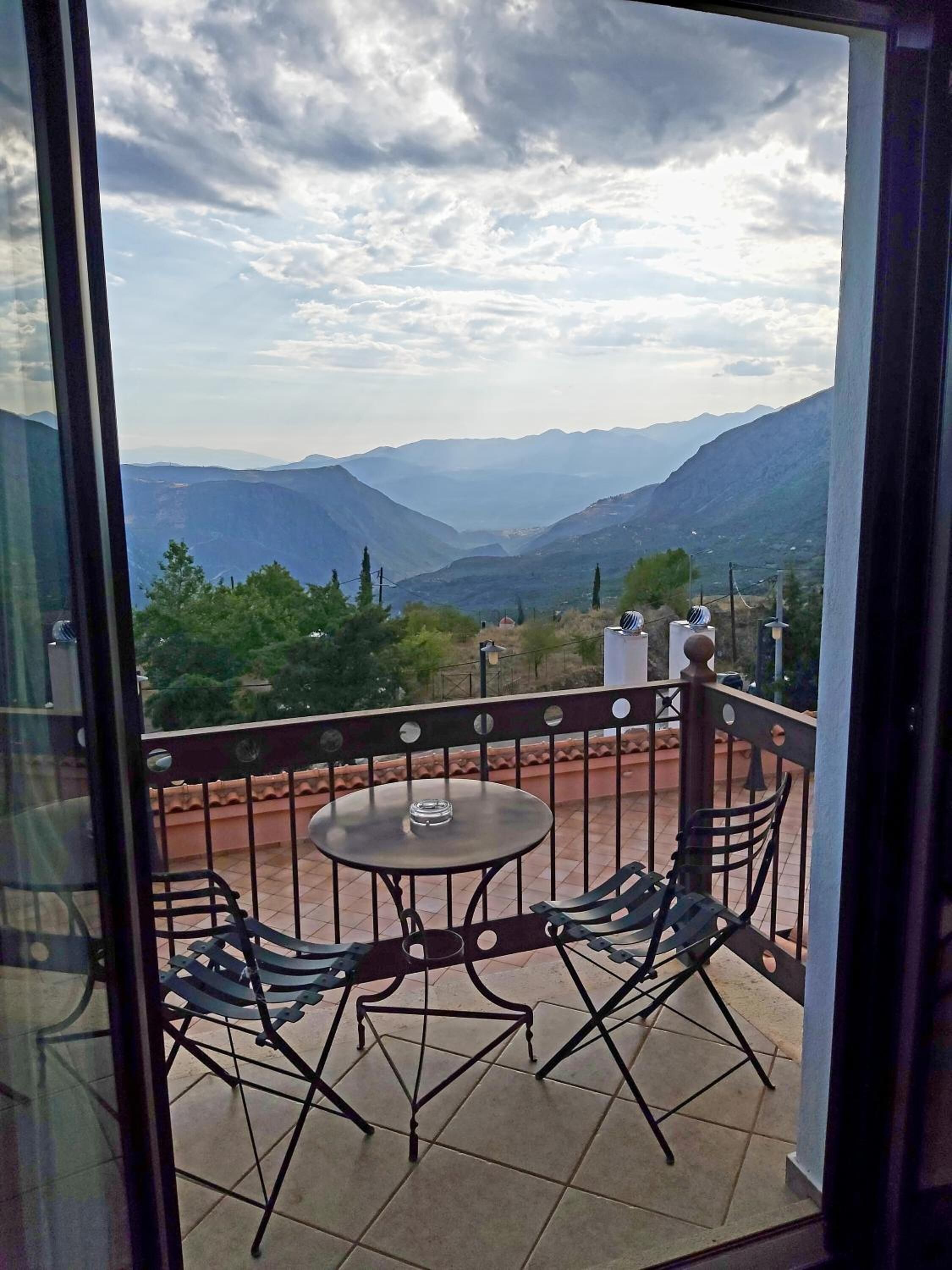 Un balcón con mesa y sillas, que ofrece vistas a montañas distantes y vegetación.