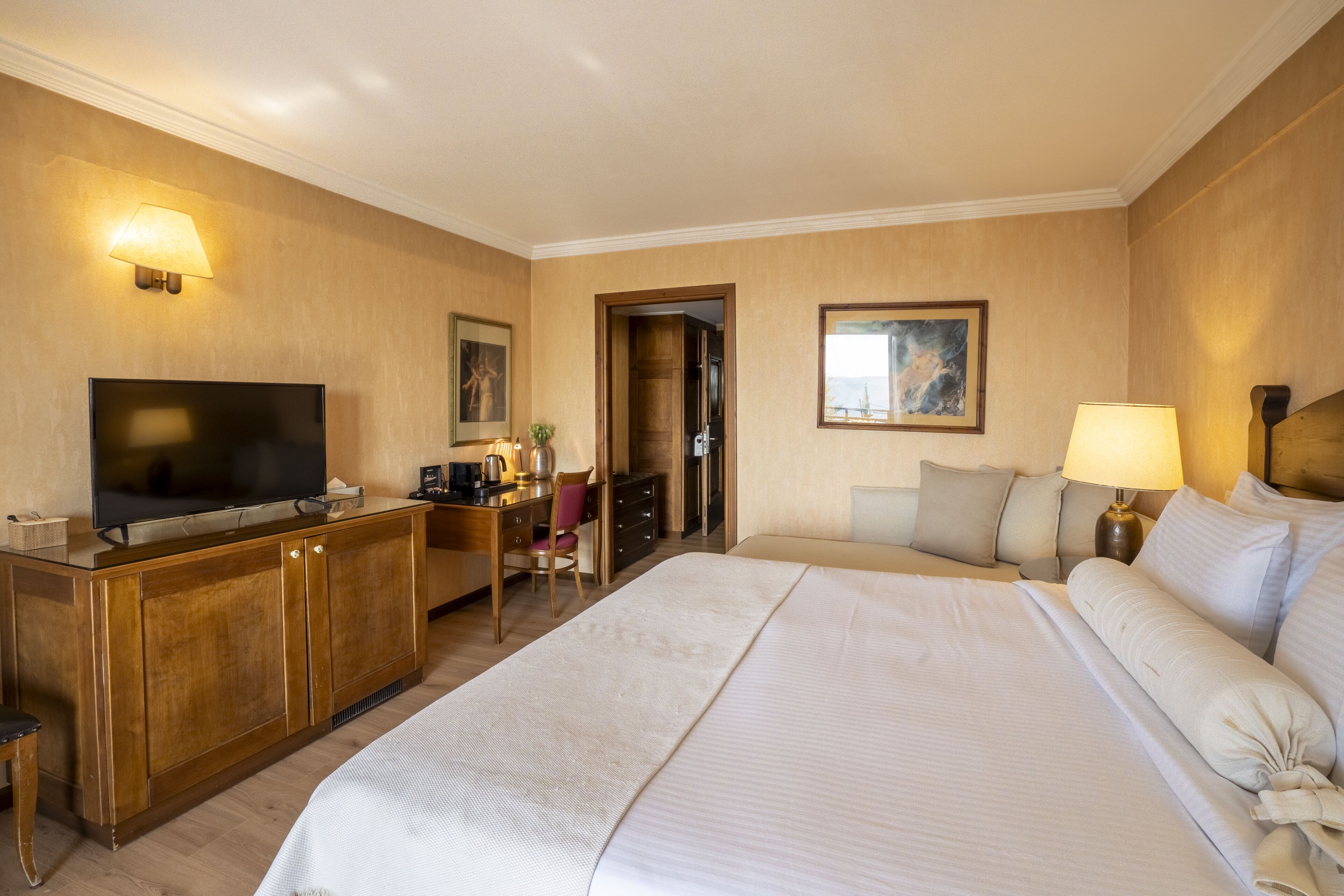 Una habitación de hotel con una cama grande, televisor, escritorio con silla y lámpara.