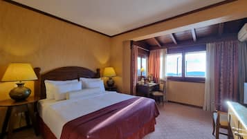 A hotel room with a large bed, two bedside lamps, a desk with a chair, and a window with curtains.