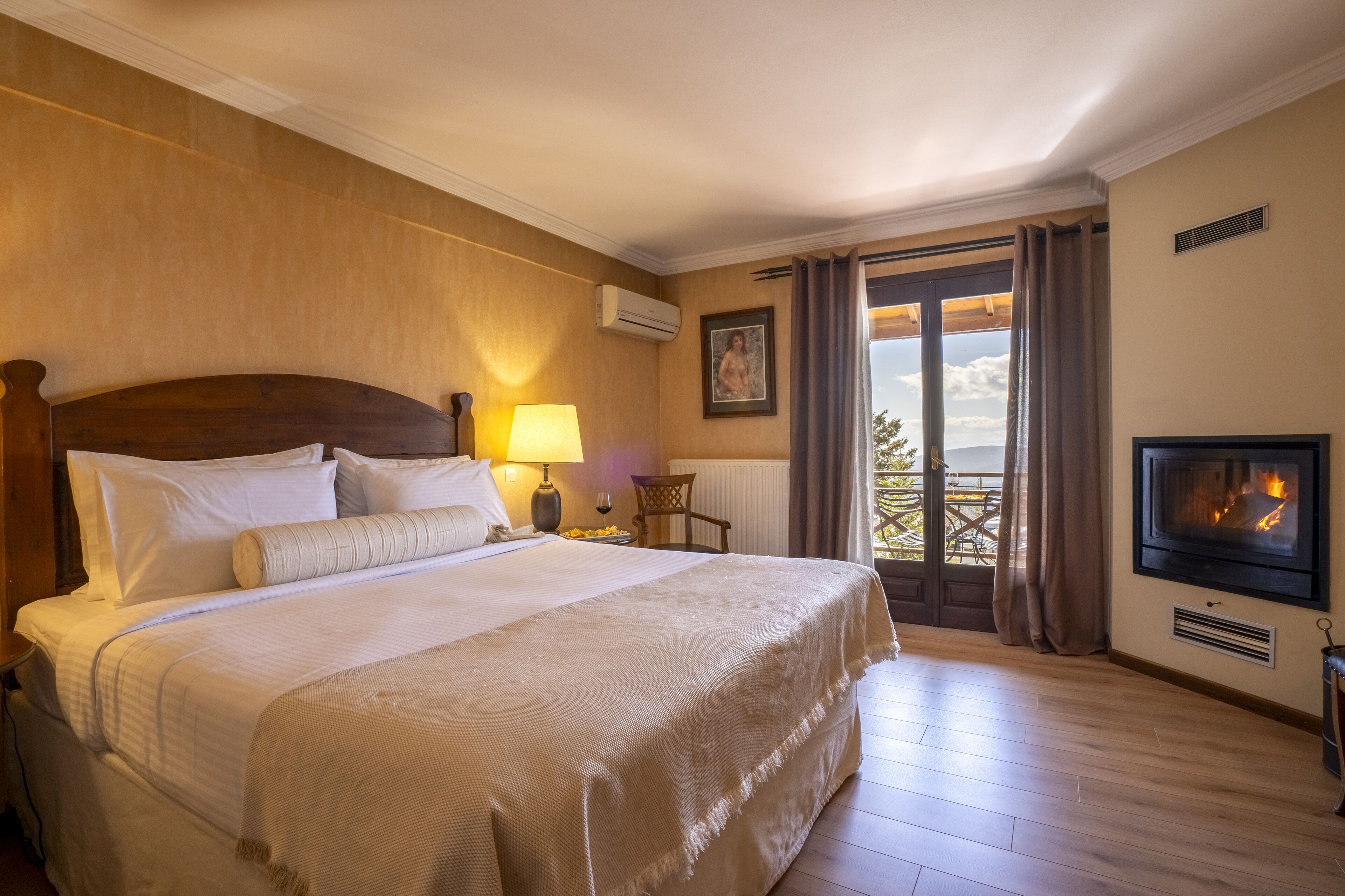 A hotel room with a large bed, a TV, a fireplace, and a balcony with a view.