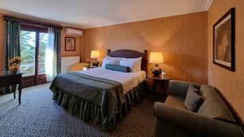 A hotel room with a large bed, two bedside tables with lamps, a sofa, a window with curtains, and a framed picture on the wall.