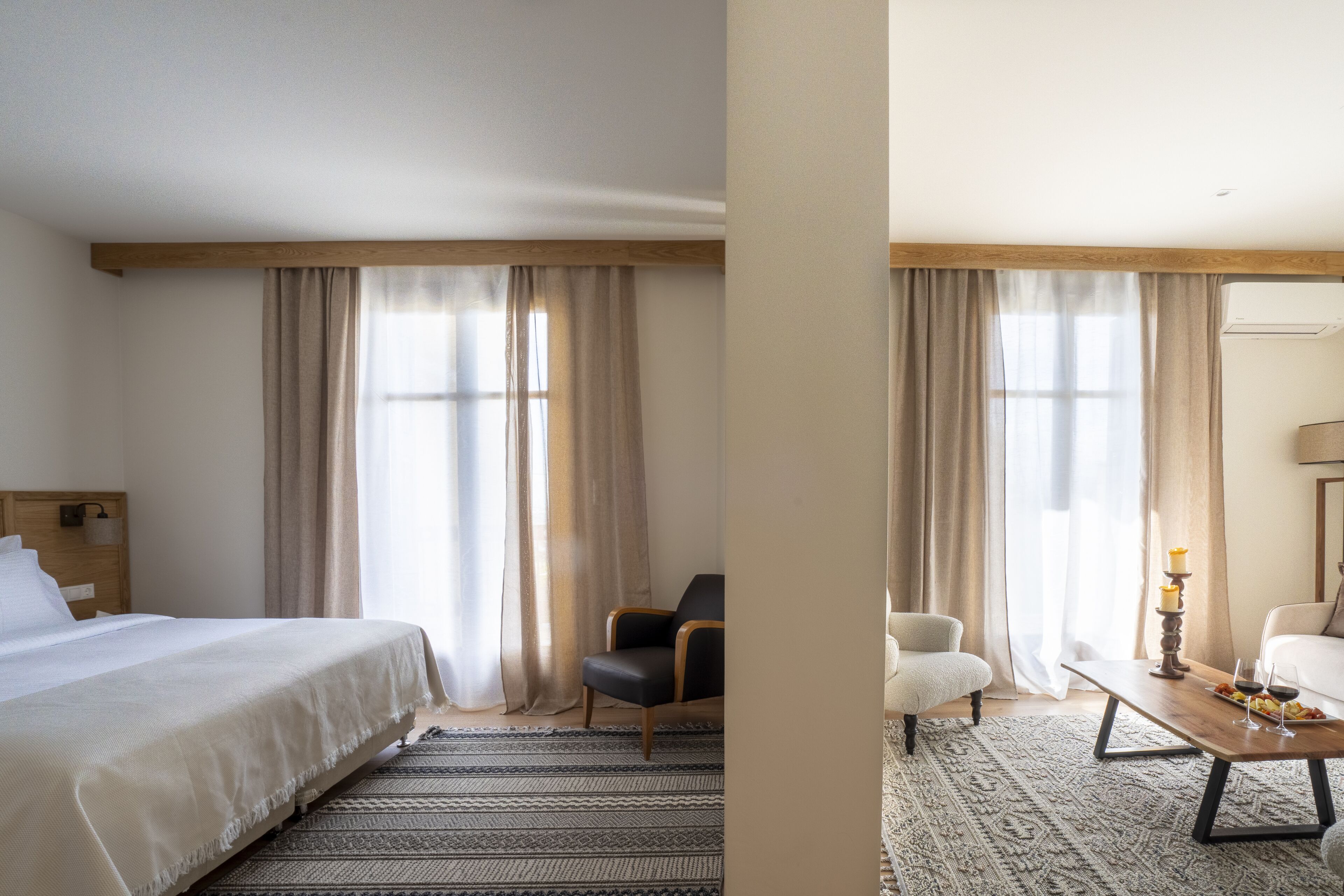 A hotel room with a bed, a chair, a sofa, a coffee table, and a dining table with a candle and wine glasses.