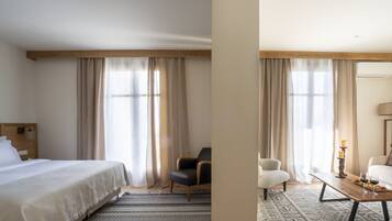 Quarto de hotel com cama, cadeira, sofá, mesa de centro e mesa de jantar, com vela e copos de vinho.