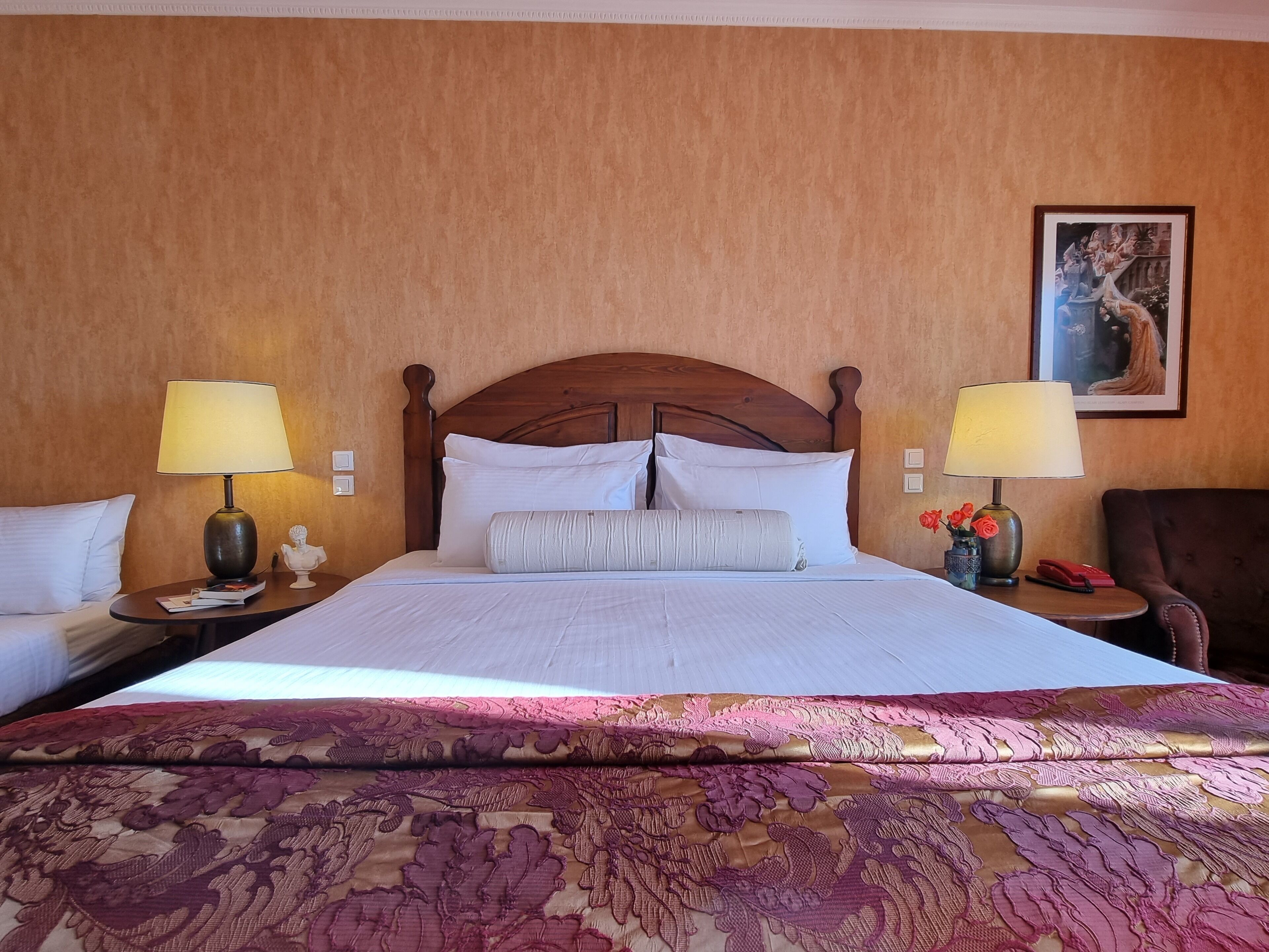 A hotel room with a large bed, two bedside tables with lamps, a wooden headboard, and a framed picture on the wall.