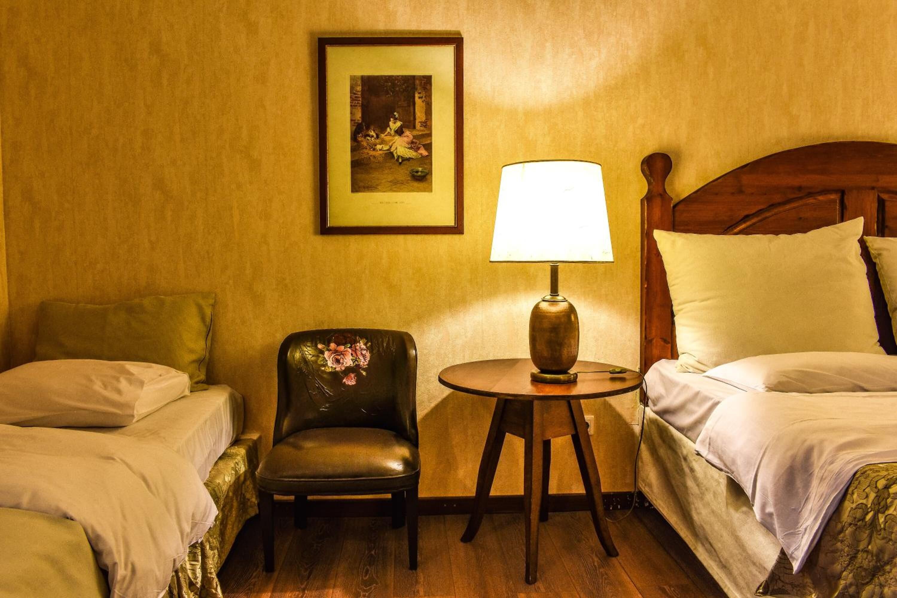 A hotel room with two beds, a chair, a table with a lamp, and a framed picture on the wall.