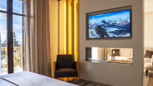 Ein Hotelzimmer mit einem großen Bett, einem an der Wand befestigten Fernseher, einem Sessel und Blick ins Freie.