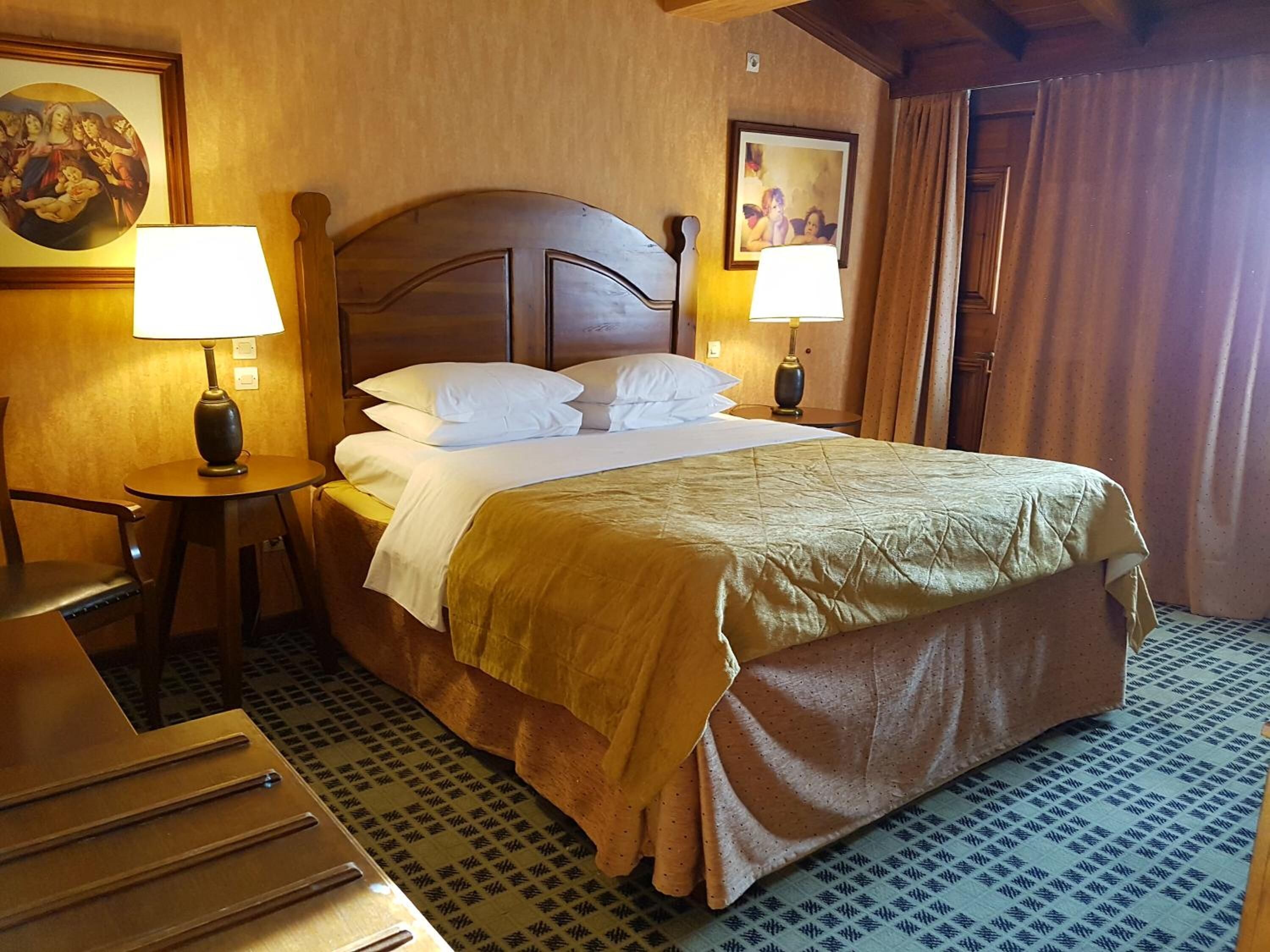Hotellihuone, jossa on suuri sänky, kaksi yöpöytää valaisimineen, puinen sängynpääty ja kuvioitu lattia.