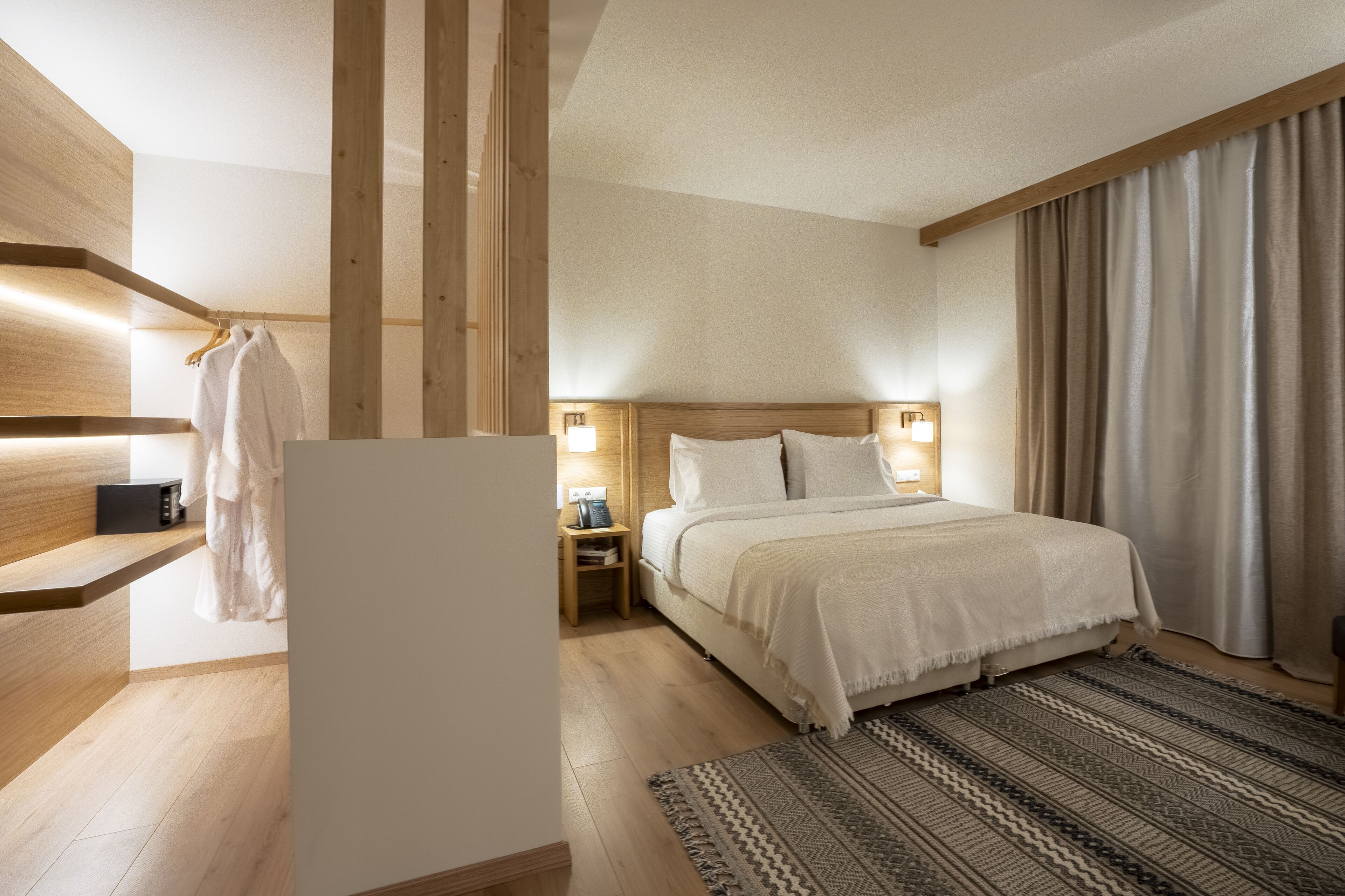 Een moderne hotelkamer met een houten vloer, een groot bed met wit beddengoed, een nachtkastje met een lamp en een opbergmantel.