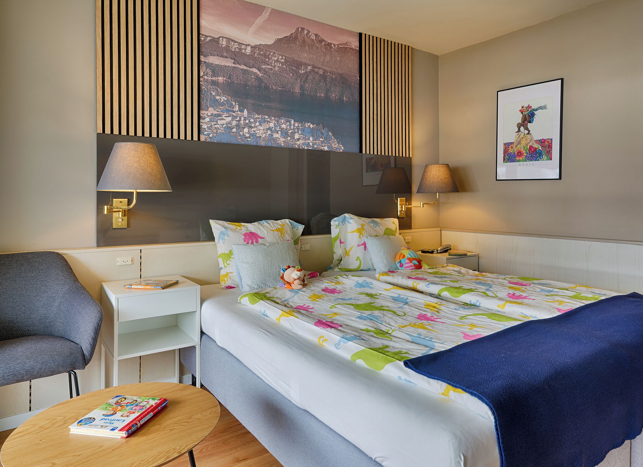Ein Hotelzimmer mit einem Bett, zwei Nachttischen, einem Sessel, einem kleinen runden Tisch und einer Wand mit einem Gemälde und einer Lampe.