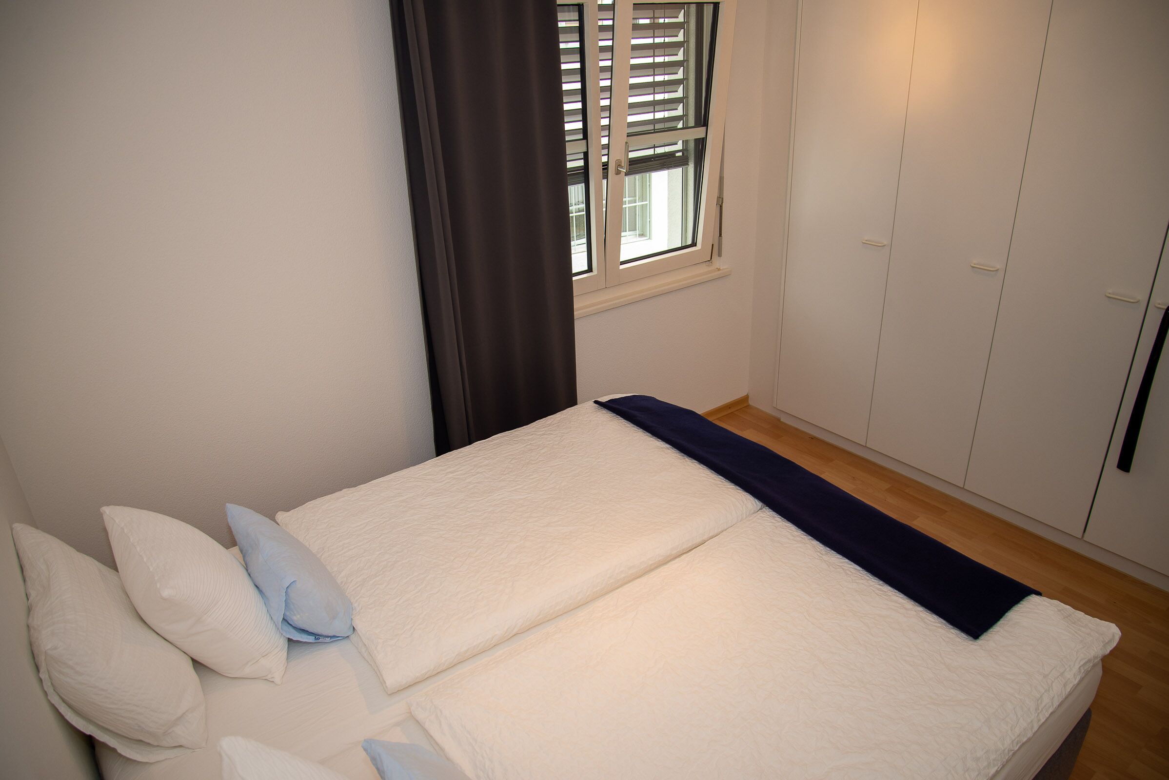 A bedroom with a bed, a window with blinds, a wardrobe, and a curtain.