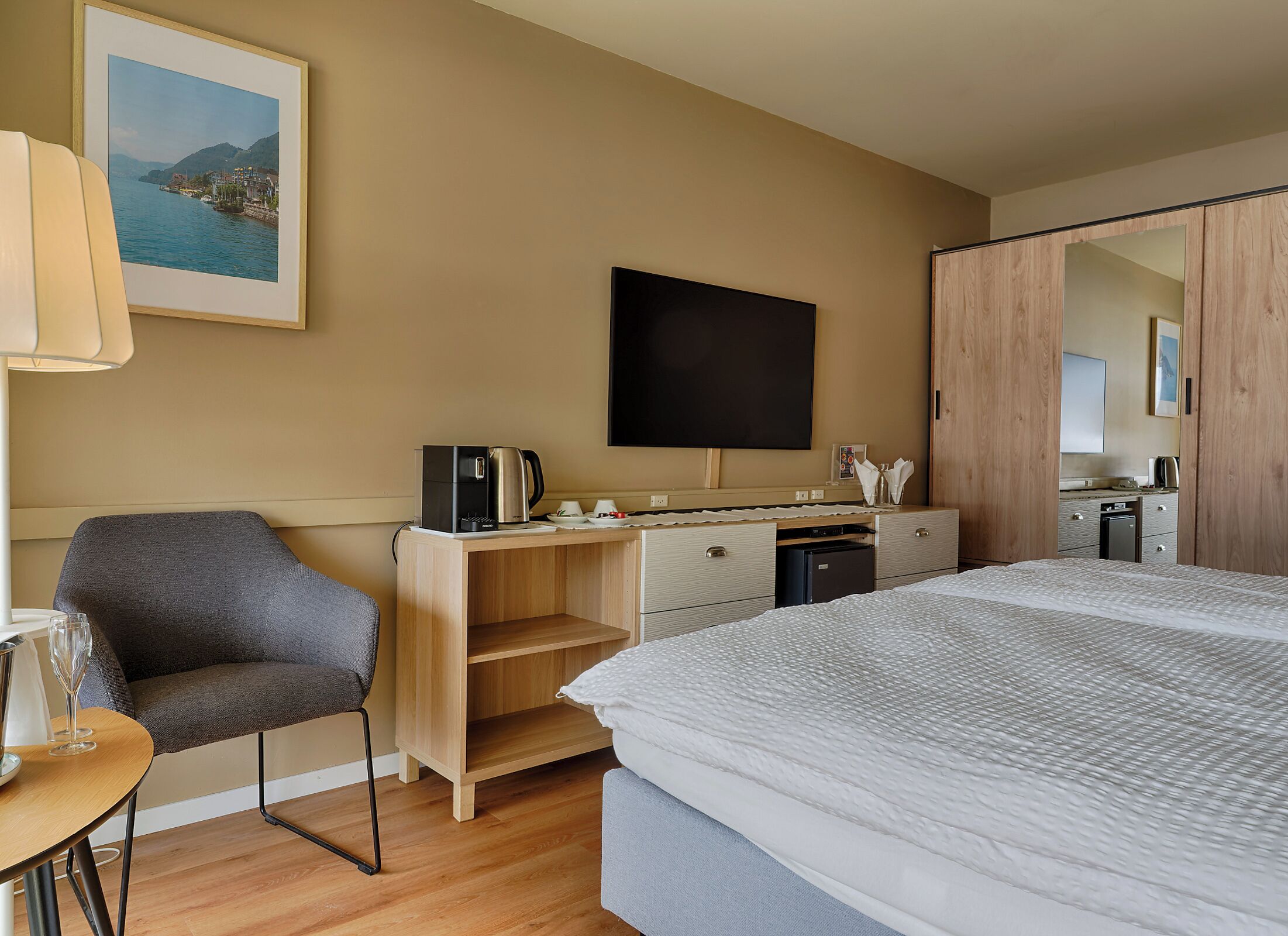 Habitación de hotel con cama, escritorio con cafetera, una silla, televisor y baño visible a través de una puerta.