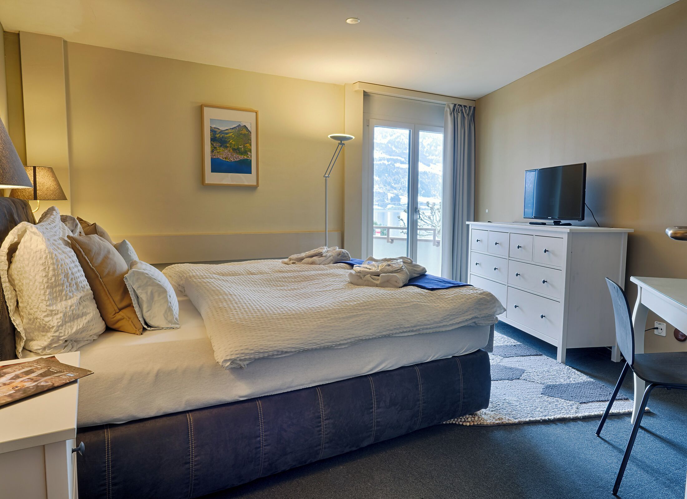 A hotel room with a bed, a desk, a television, a lamp, and a window with a view.