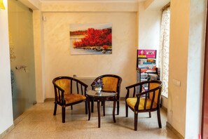A room with a painting of a landscape, two wooden chairs, a small table, and a bookshelf with magazines. - Cantemir (Bucharest)