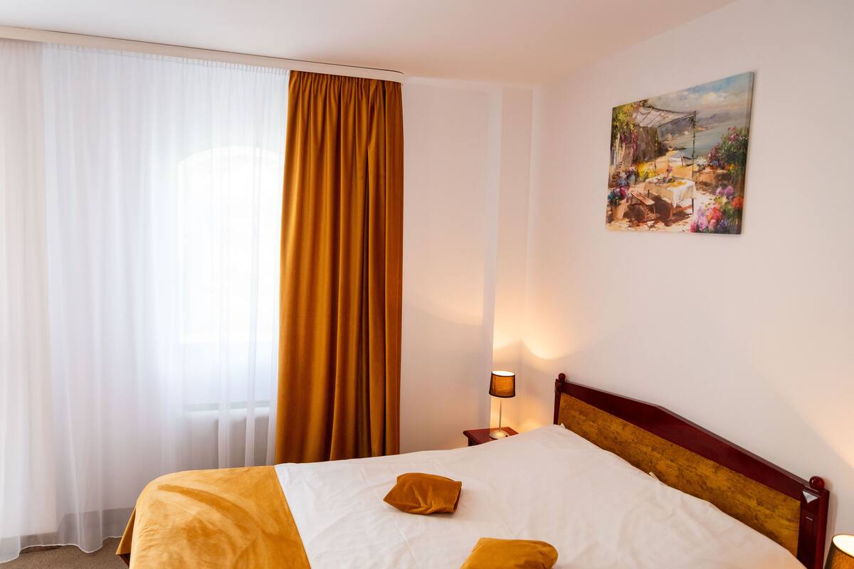 A hotel room with a bed, a nightstand, a lamp, a painting on the wall, and a window with curtains.