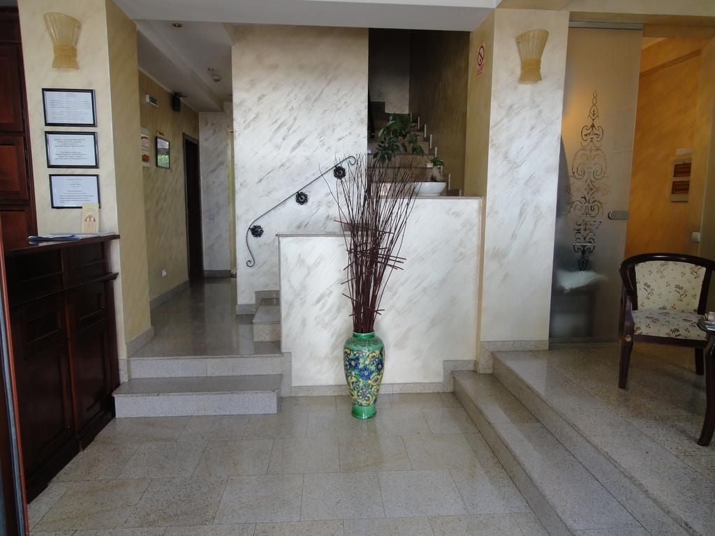 Un área de recepción con una escalera de mármol, un jarrón verde con ramas y una silla de madera.