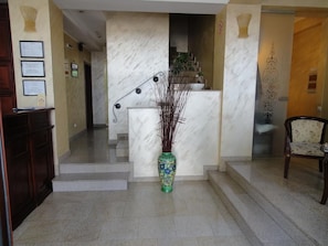 A reception area with a marble staircase, a green vase with branches, and a wooden chair. - Cantemir (Bucharest)