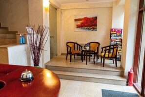 Un espace d’accueil comprenant un comptoir de réception, deux chaises, une table, un tableau et un escalier.