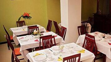 A dining area with tables set for four, each with white tablecloths, red chairs, and a vase of flowers.