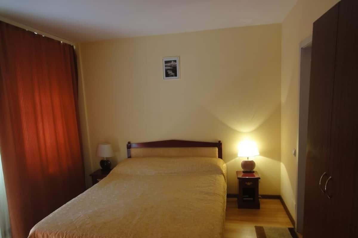 A hotel room with a bed, a nightstand with a lamp, a picture on the wall, and a wardrobe.
