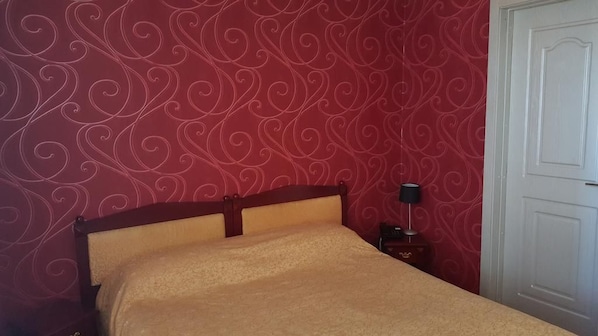 Un lit avec une tête de lit en bois, une table de chevet avec une lampe et un mur décoré d’un motif rouge.