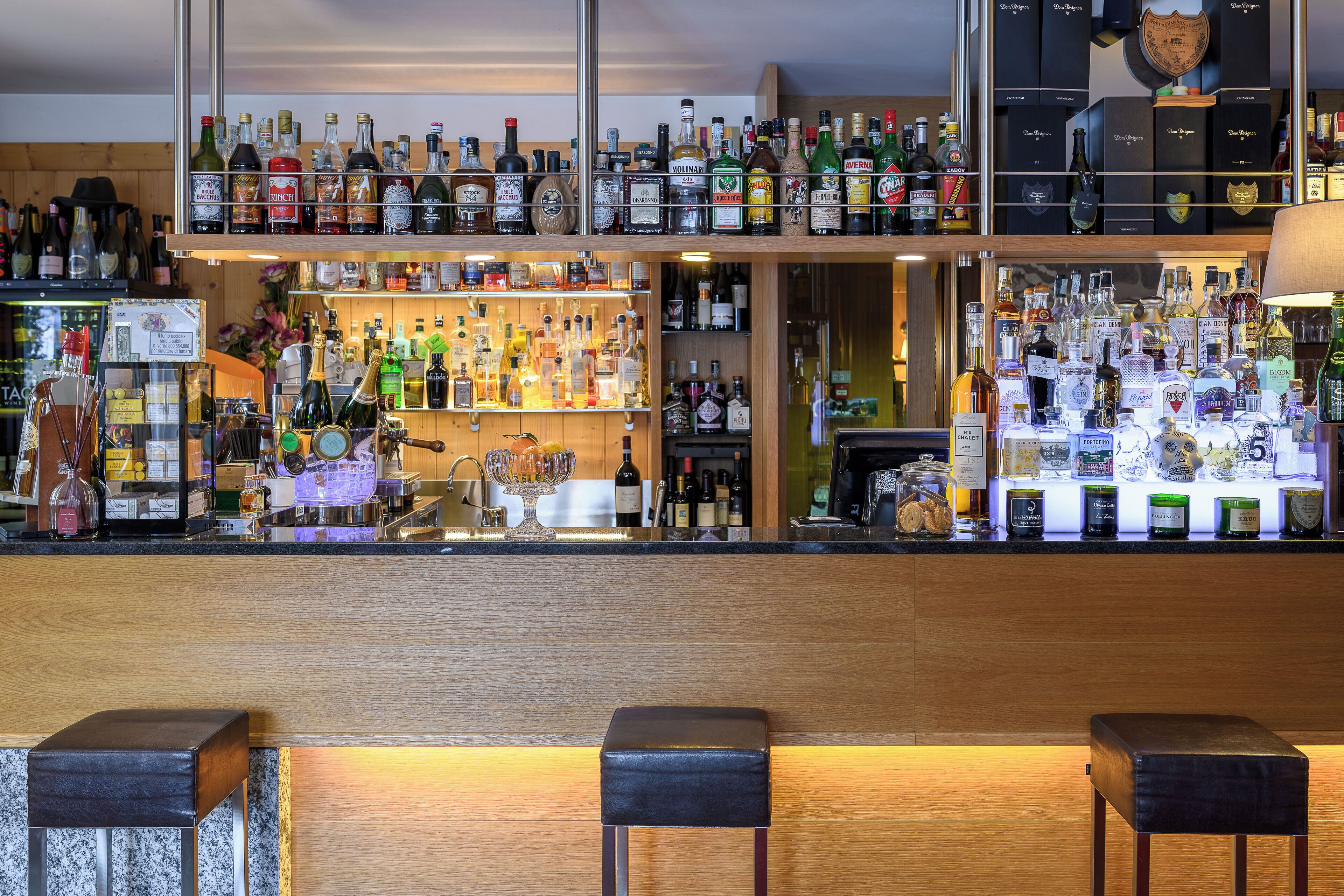 Un bar con numerose bottiglie di liquori, un bancone in legno e due sgabelli.