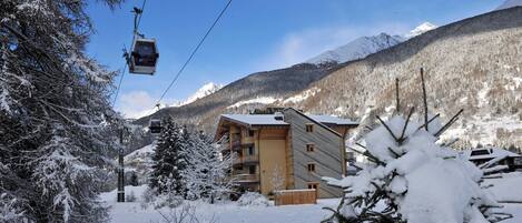 A snow-covered mountain area with a ski lift, a lodge, and a view of snow-capped mountains.
