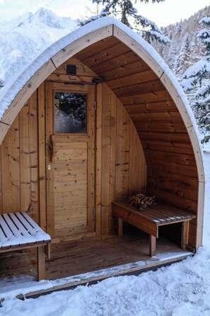 A wooden cabin with a bench outside, surrounded by snow-covered mountains. - Hotel Garnì Pegrà (Ponte di Legno)