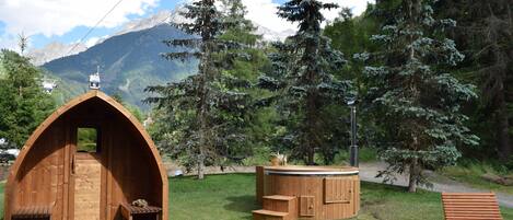 Una cabaña de madera con techo inclinado, un banco de madera y un jacuzzi en una zona montañosa.