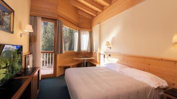 Habitación de hotel con techo de madera, cama con sábanas blancas, escritorio con televisor y ventana con cortinas.