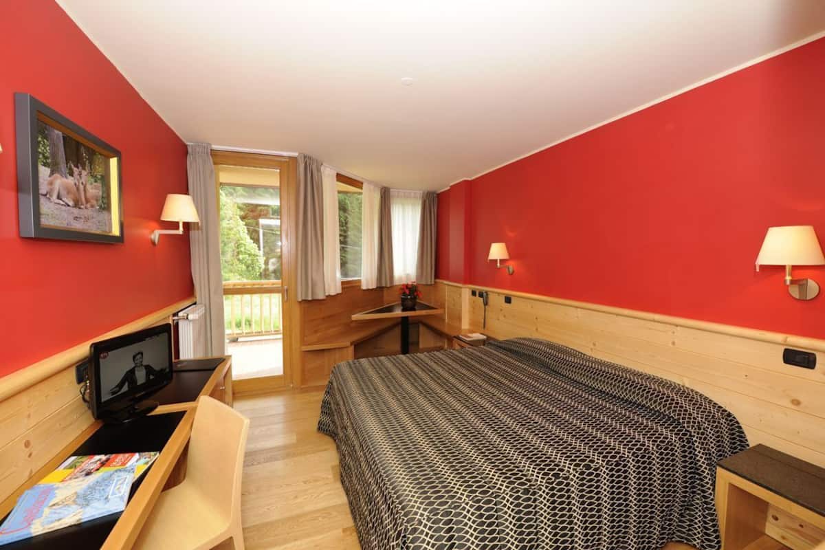 A room with a bed, a desk with a computer, a chair, and a window with curtains.