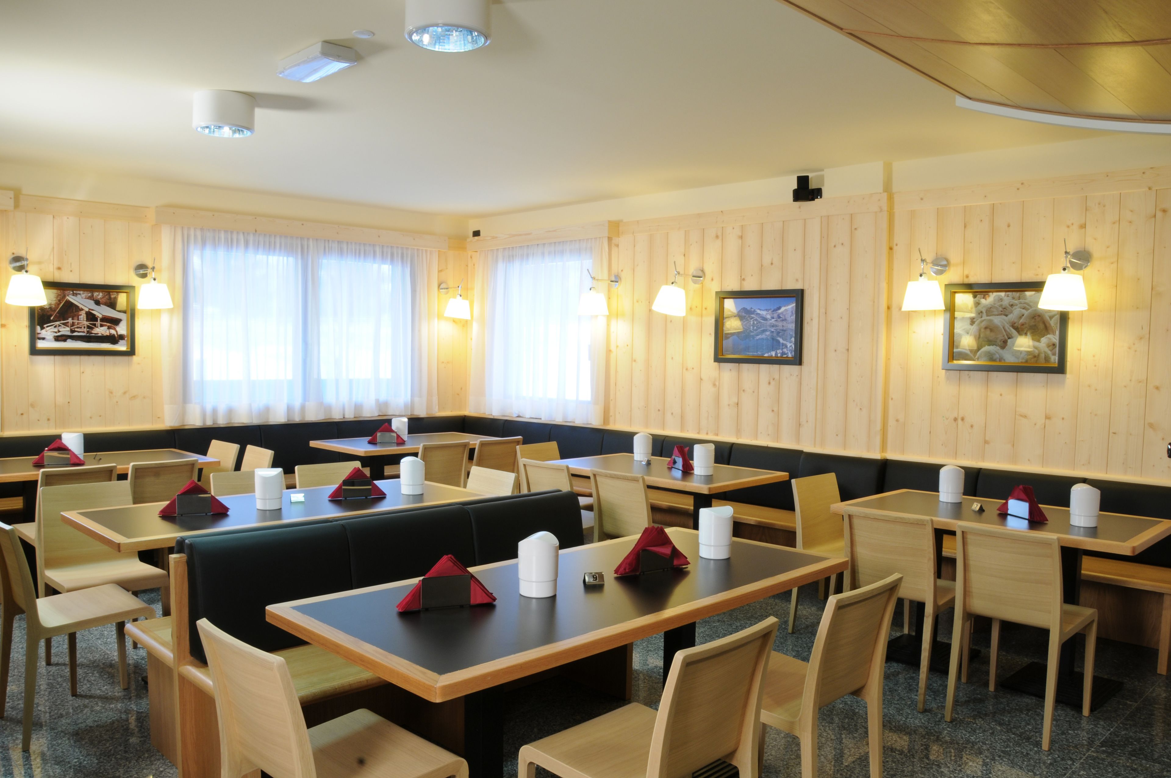 Een restaurant met houten lambrisering, verschillende tafels en zitjes, en wandlampen.