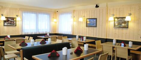Een restaurant met houten lambrisering, verschillende tafels en zitjes, en wandlampen.