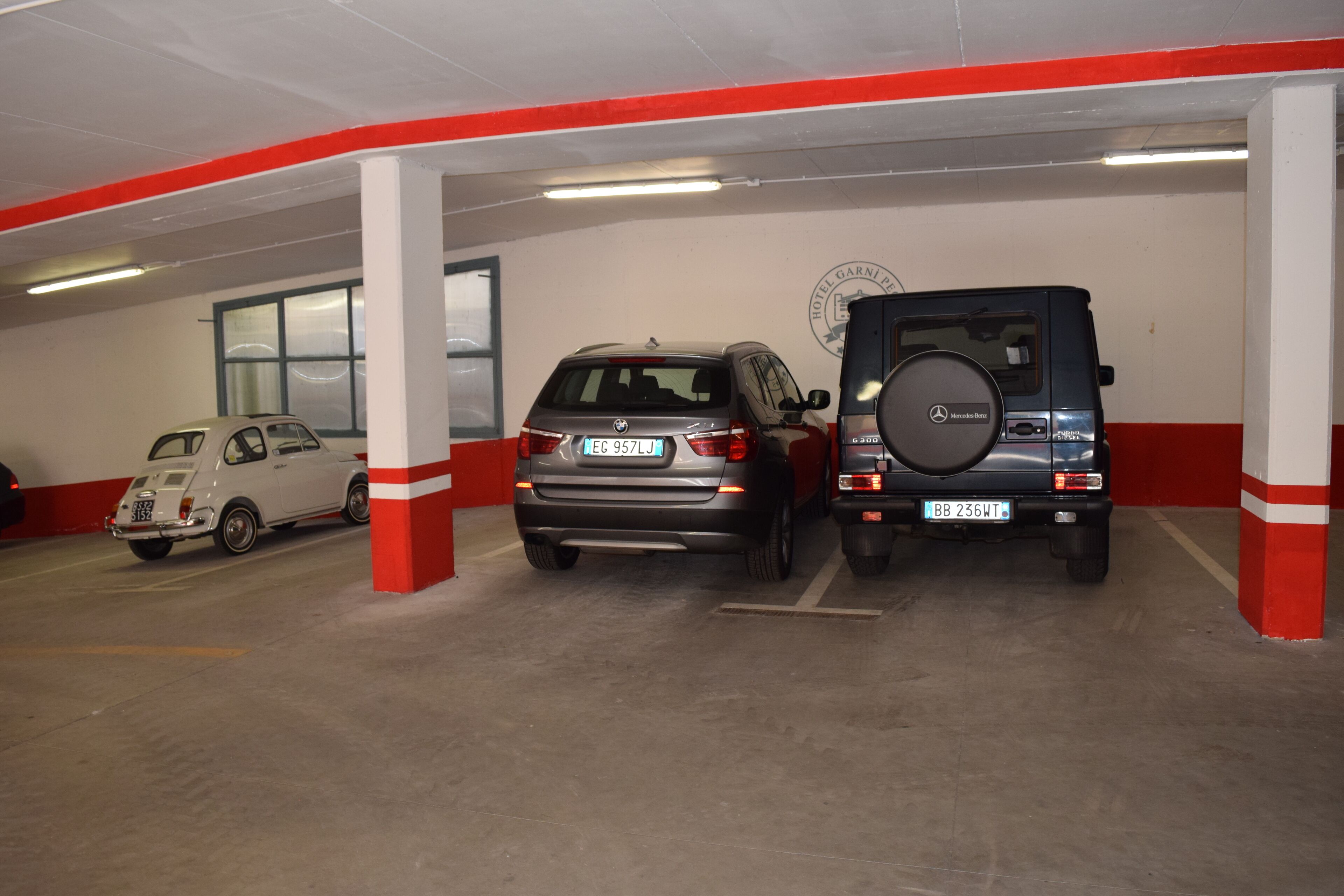 A parking garage with three vehicles: a white car, a gray SUV, and a black SUV.