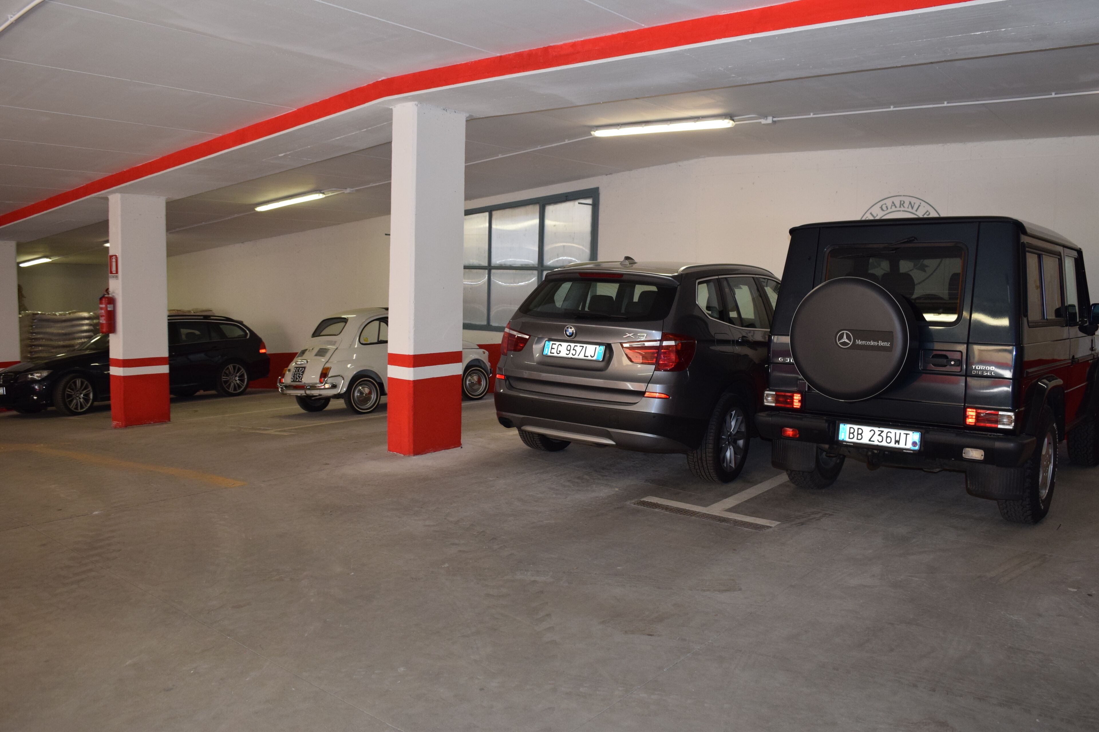 Een parkeergarage met meerdere auto's, waaronder een zwarte Mercedes-Benz SUV en een zilveren SUV.