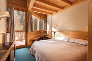 A wooden cabin bedroom with a bed, bedside table, lamp, and a view of the forest through the window. - Hotel Garnì Pegrà (Ponte di Legno)
