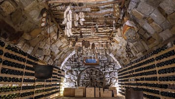 A cellar with stone walls, wooden racks, and hanging wine bottles.