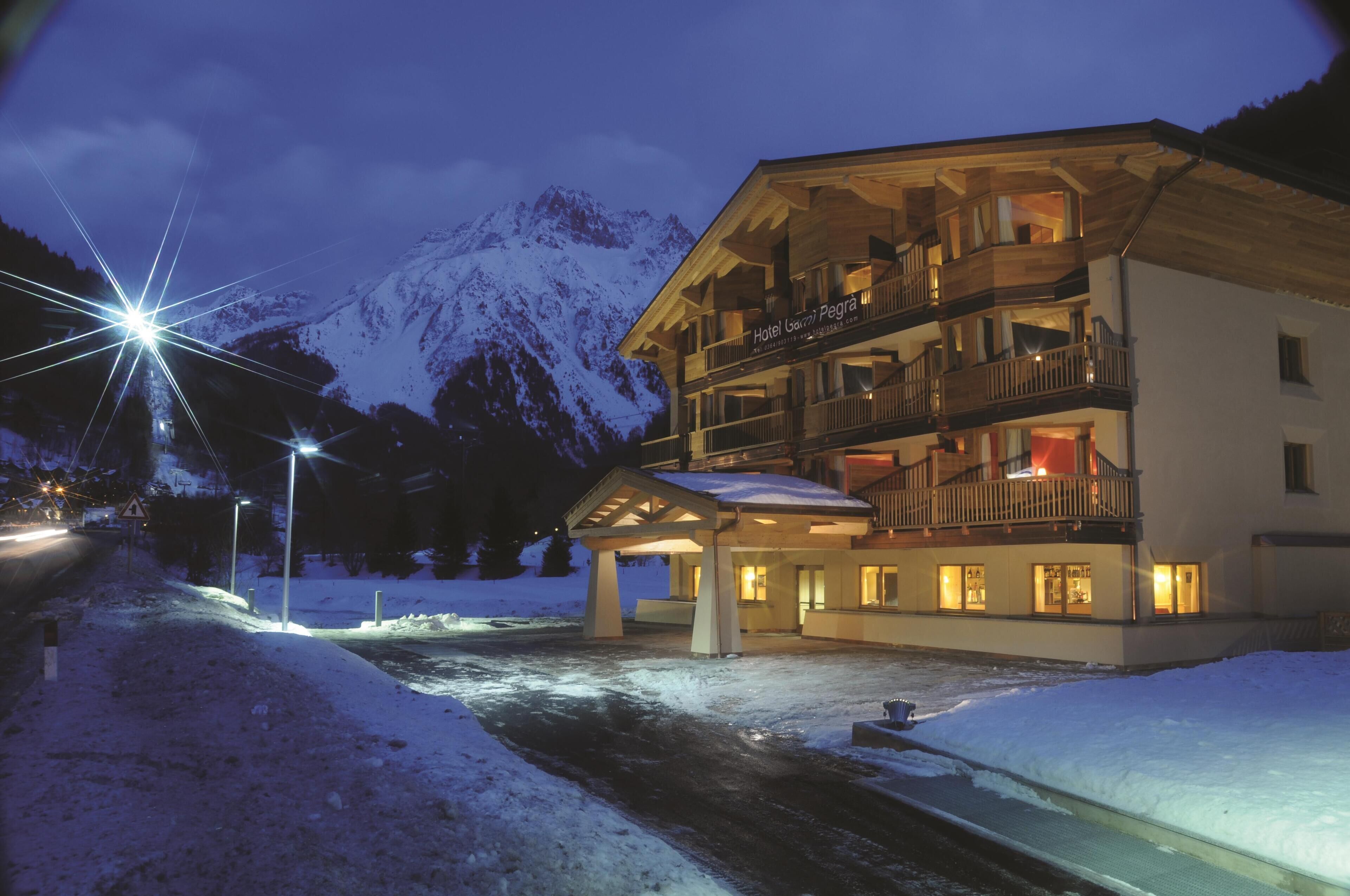 A multi-story hotel with balconies, a covered entrance, and a view of snow-covered mountains.