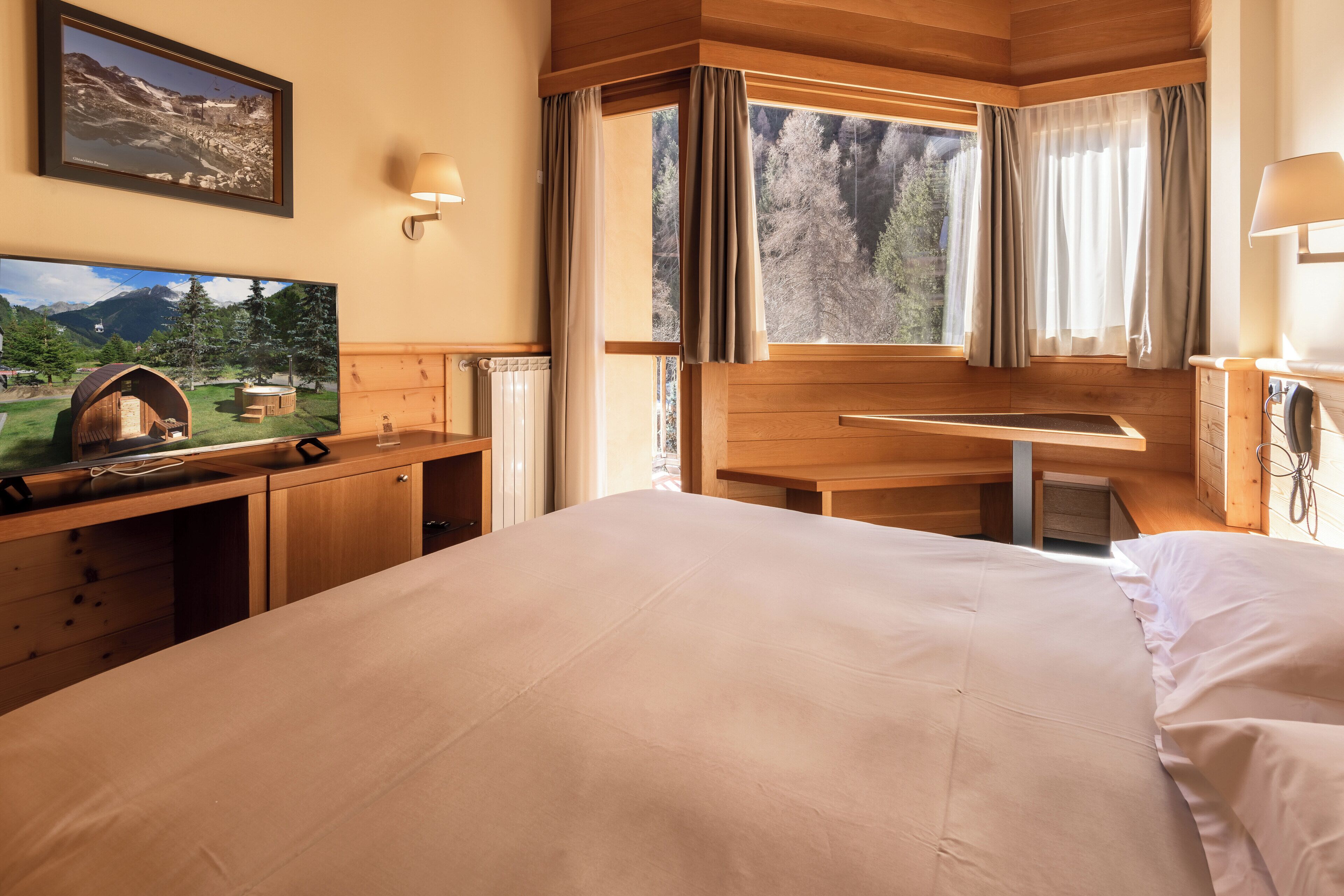 A hotel room with a bed, a desk with a computer, a TV, and a window with curtains.