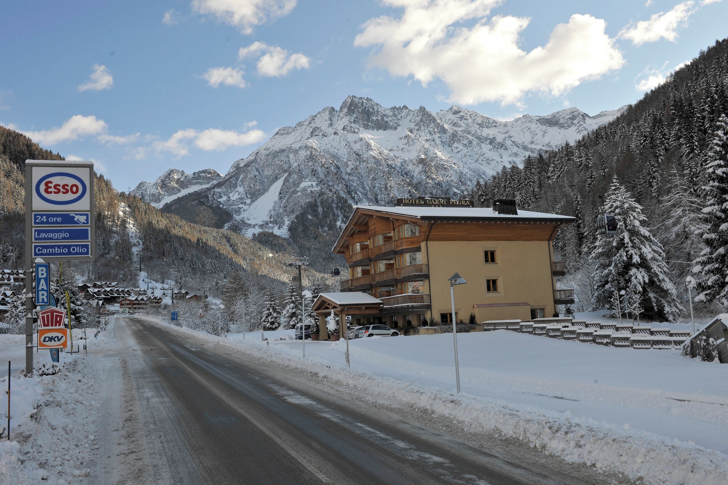 A hotel with a mountain backdrop, a sign for a bar, and a sign for a 24-hour service.