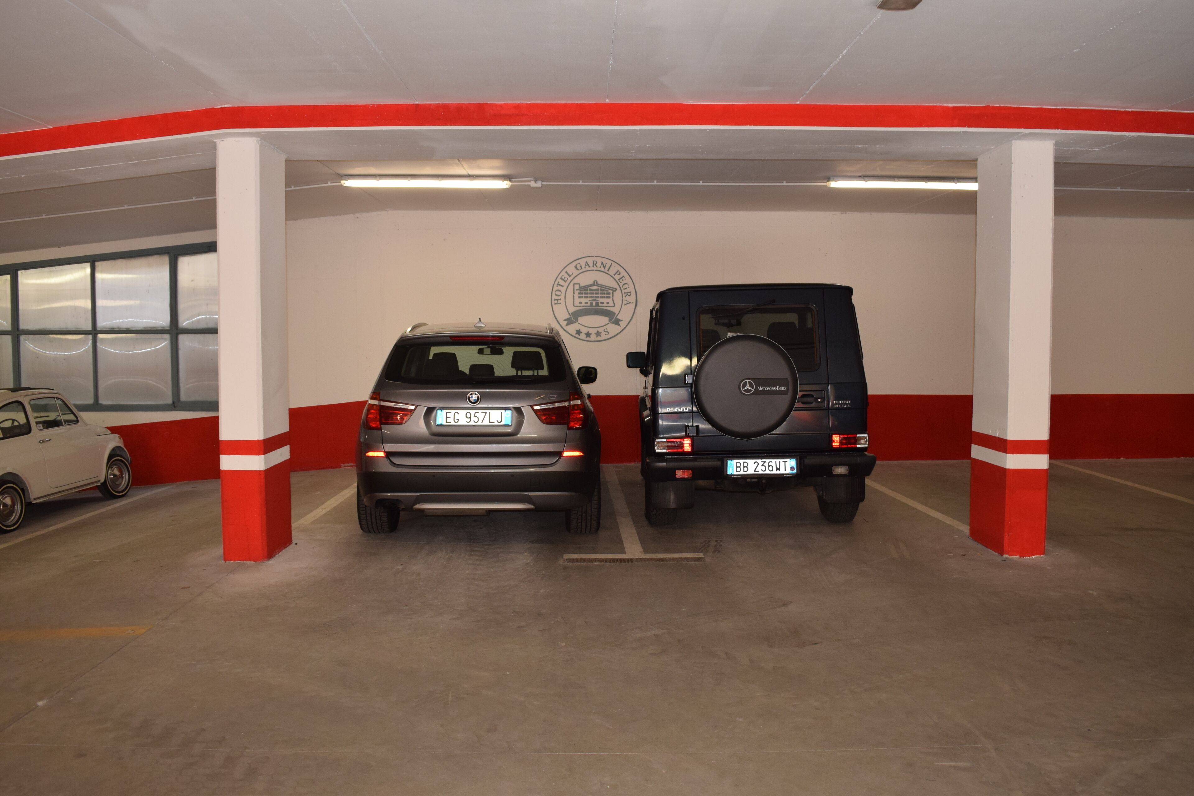 Un estacionamiento con dos coches aparcados bajo pilares blancos y rojos.