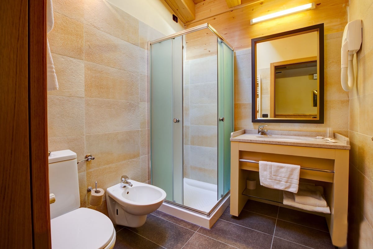 A bathroom with a glass shower enclosure, a toilet, a bidet, a sink with a mirror, and a towel rack.