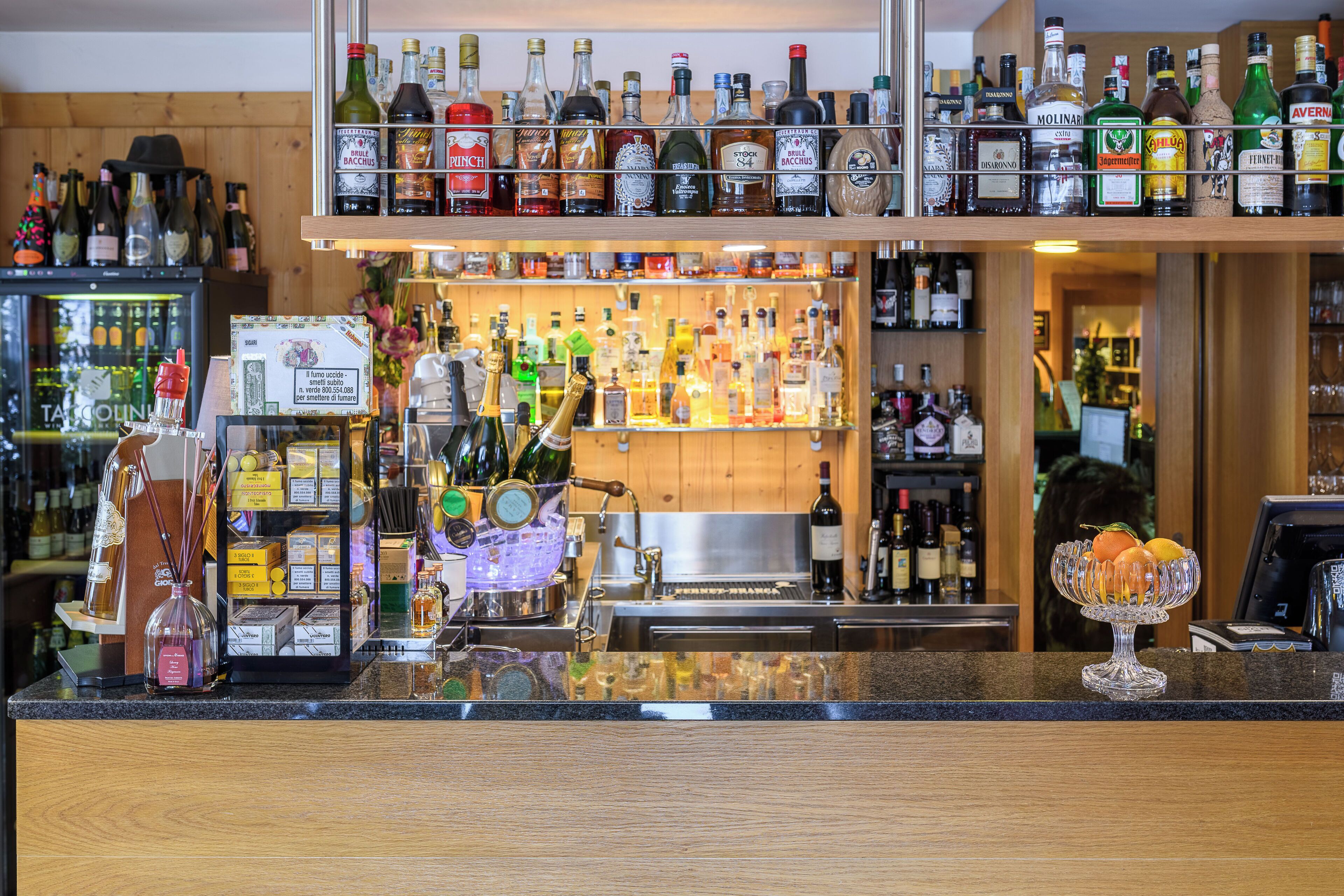 Una zona de bar con estantes llenos de botellas de licores, una caja registradora y un frutero decorativo.