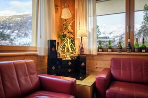 A cozy room with a view of snow-covered mountains, a fireplace with a decorative tree, and a shelf with bottles. - Hotel Garnì Pegrà (Ponte di Legno)