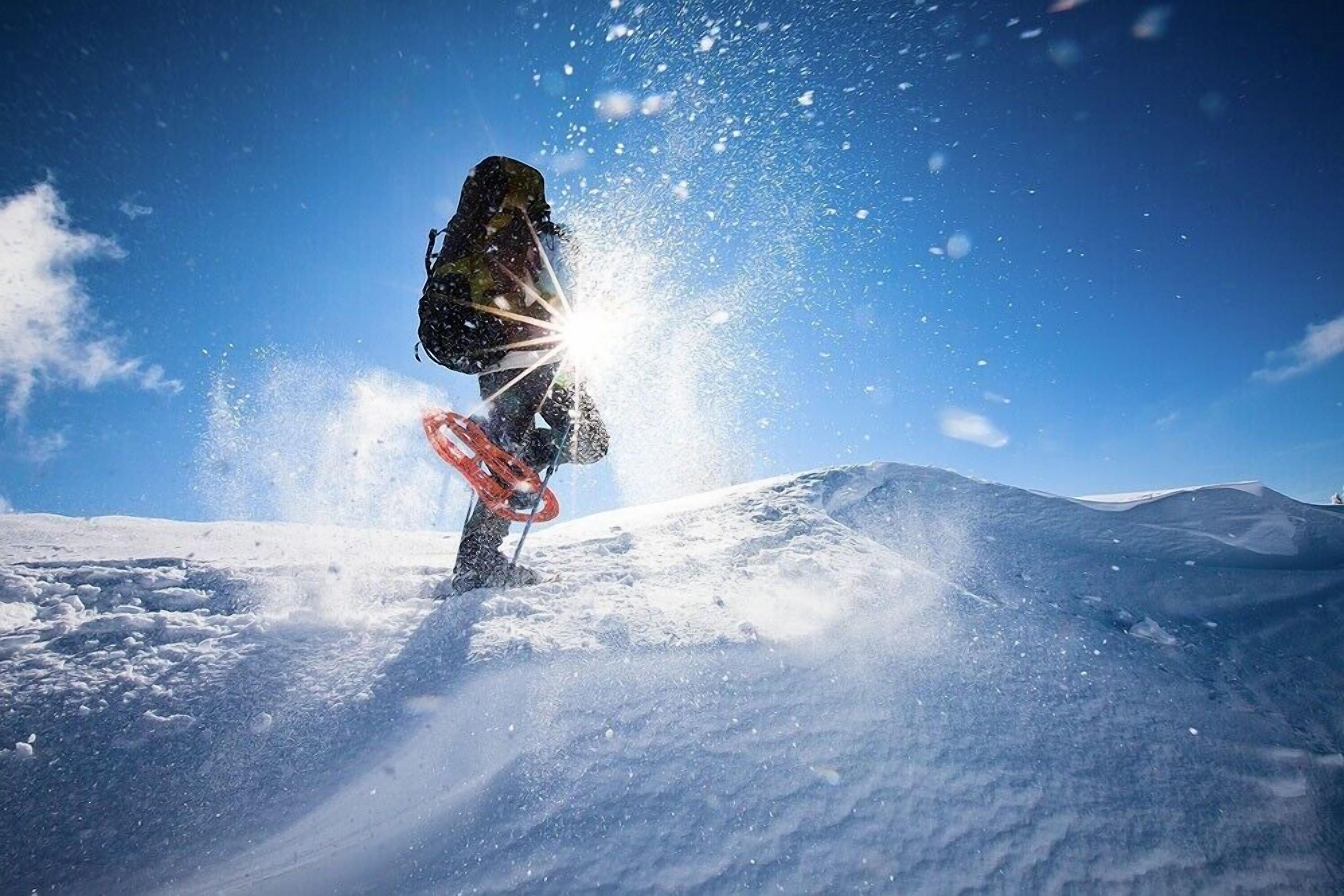 En snowboardåkare i farten på en snötäckt sluttning med en klarblå himmel i bakgrunden.