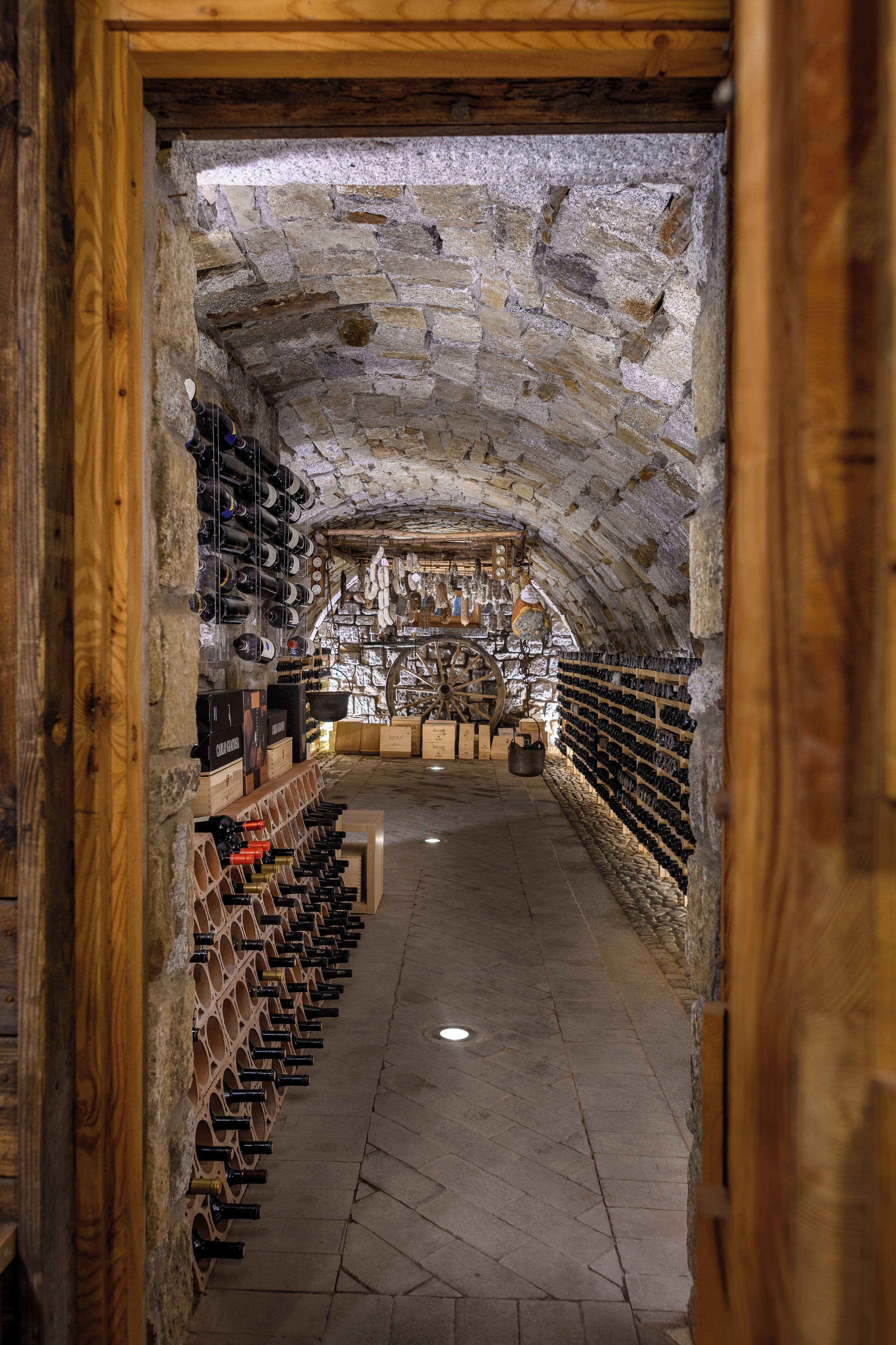 A stone-walled wine cellar with wooden racks and shelves holding wine bottles.