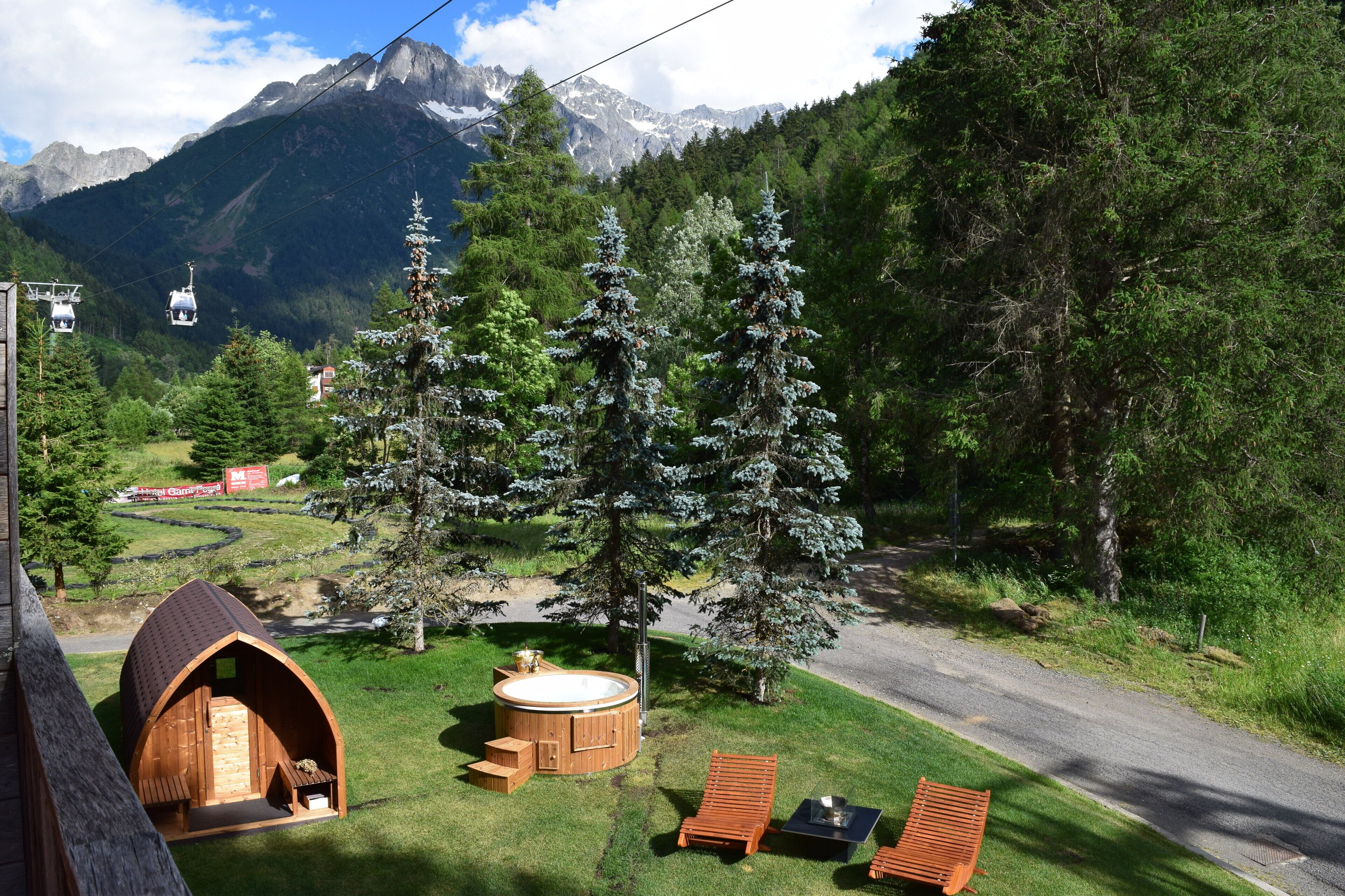 Une cabane en bois dotée d’un bain à remous et de chaises longues, située dans une zone boisée avec une vue sur les montagnes.