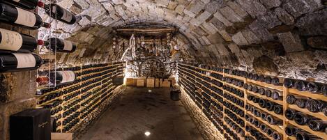 Una bodega con paredes de piedra y estanterías de madera llenas de botellas de vino.